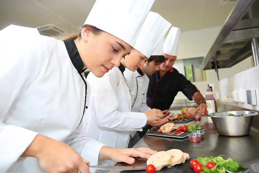 Drei junge Menschen in Kochkleidung und ein Ausbilder bereiten das Essen vor Drei junge Menschen in Kochkleidung und ein Ausbilder bereiten das Essen vor